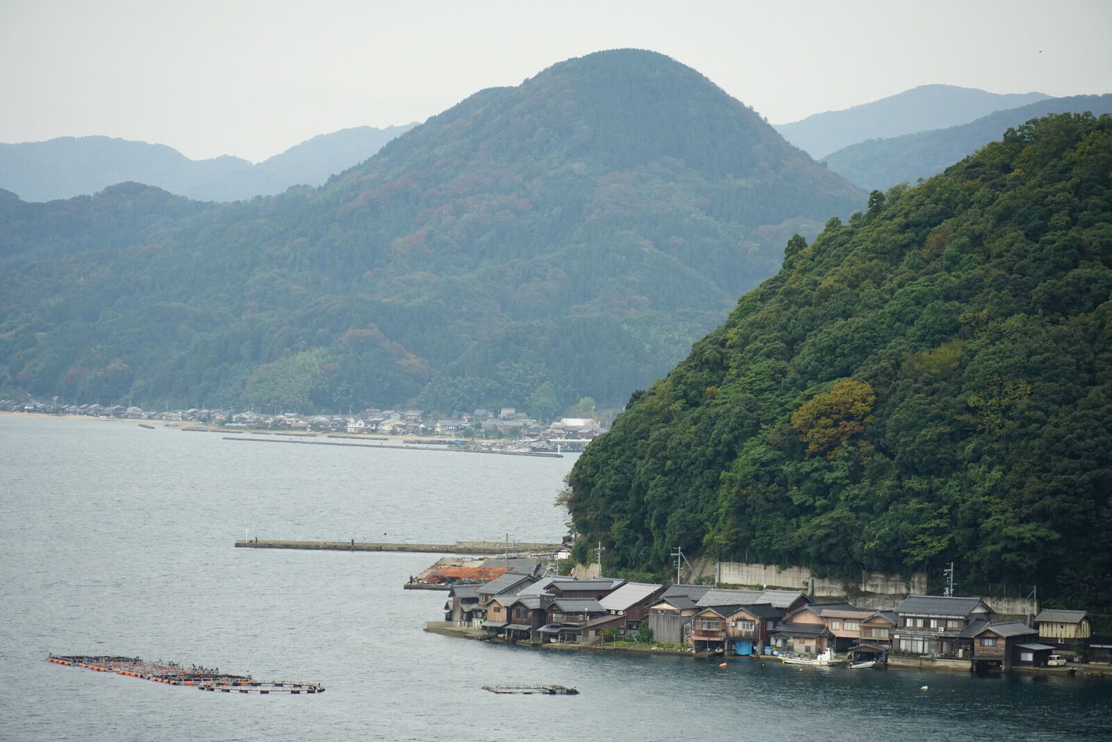 Wide view of the funaya coast with the forested headland and layered mountain ridges fading into the haze