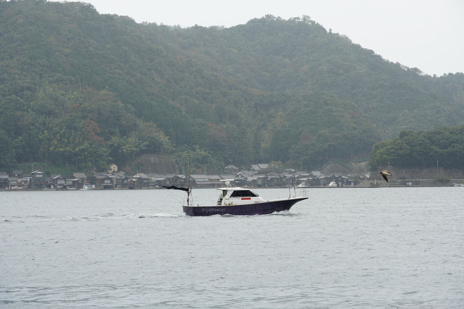A lone fishing boat on the misty waters of Ine Bay with funaya silhouettes in the background