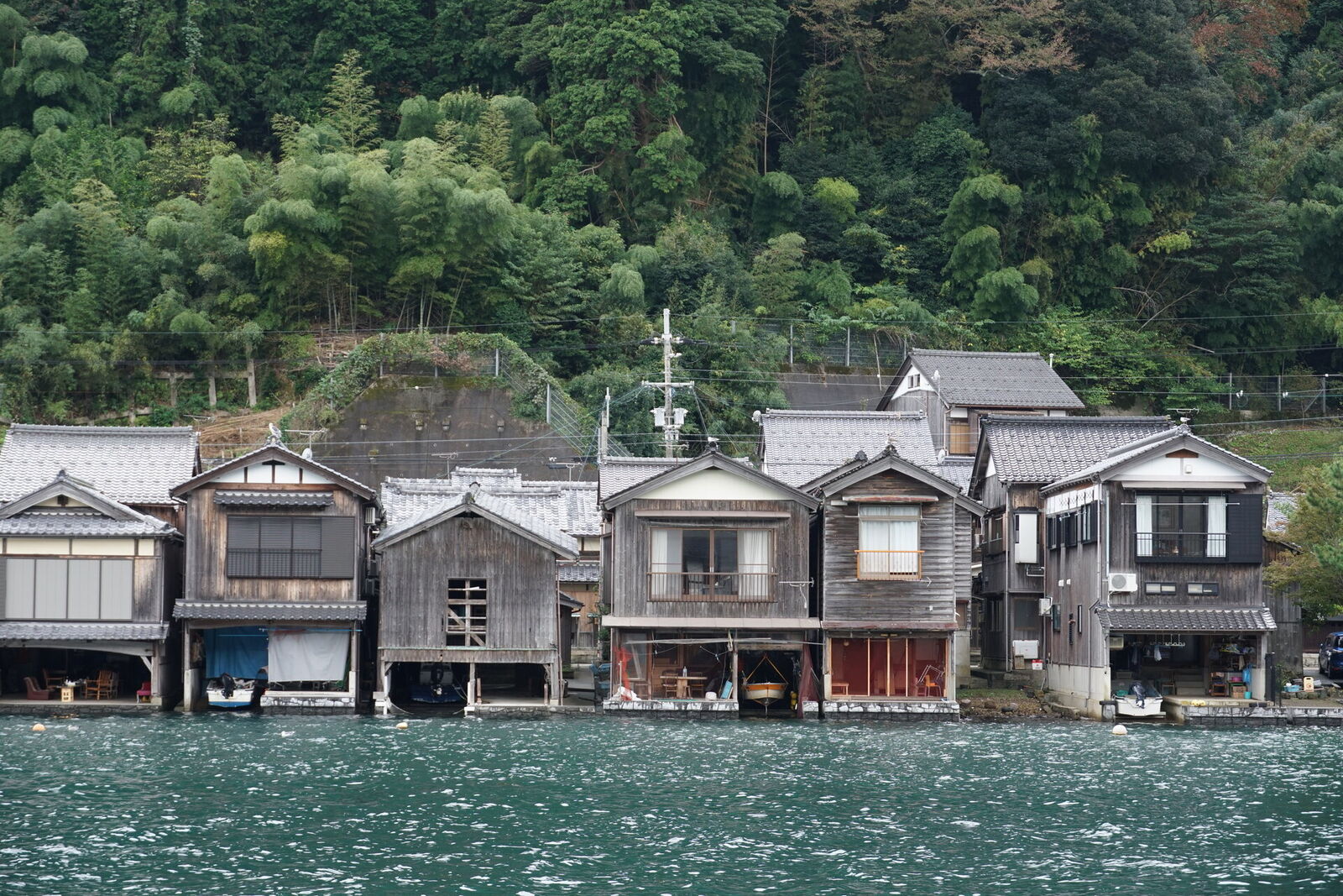 Close-up of funaya garages from the water showing the open boat storage at water level, sparkling sea in the foreground