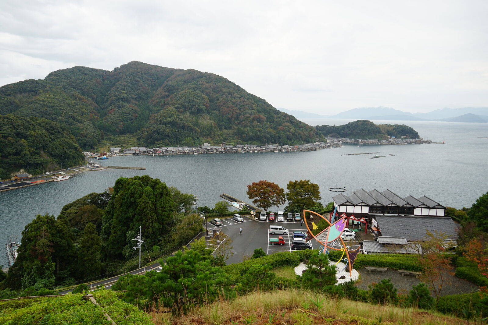 The Michi no Eki hilltop parking with a view down to the bay, colorful art sculpture, and funaya village below