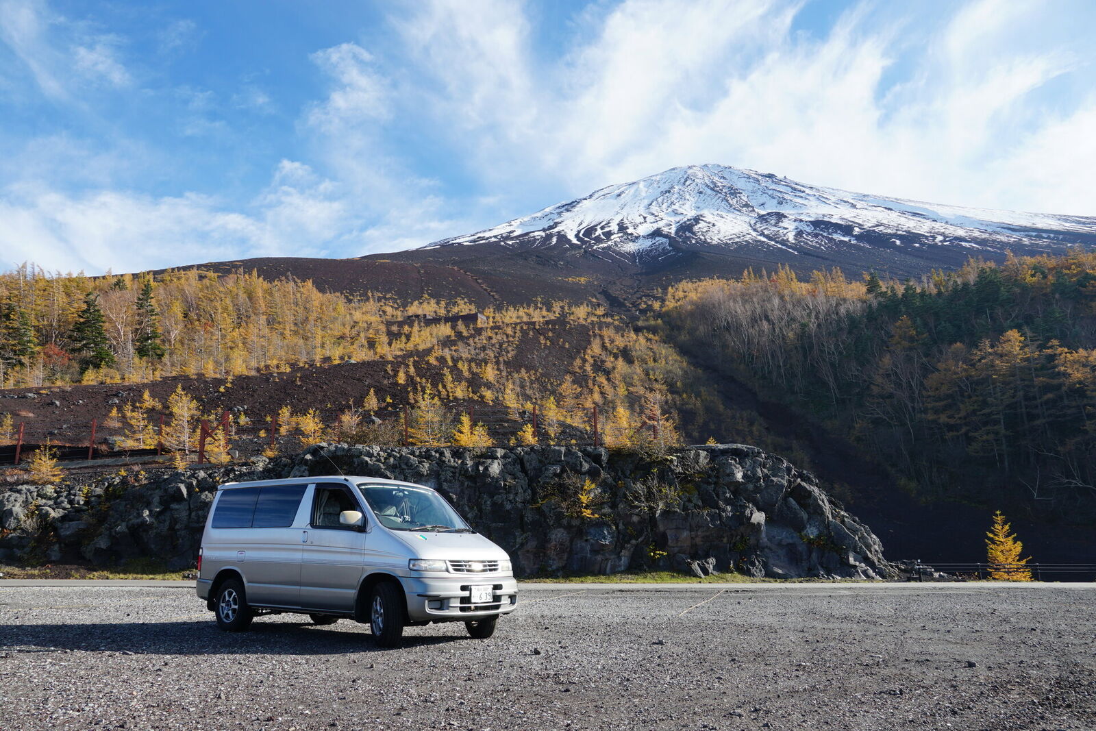 Campervan parked at the base of Mount Fuji with golden autumn larch trees and snow-capped peak