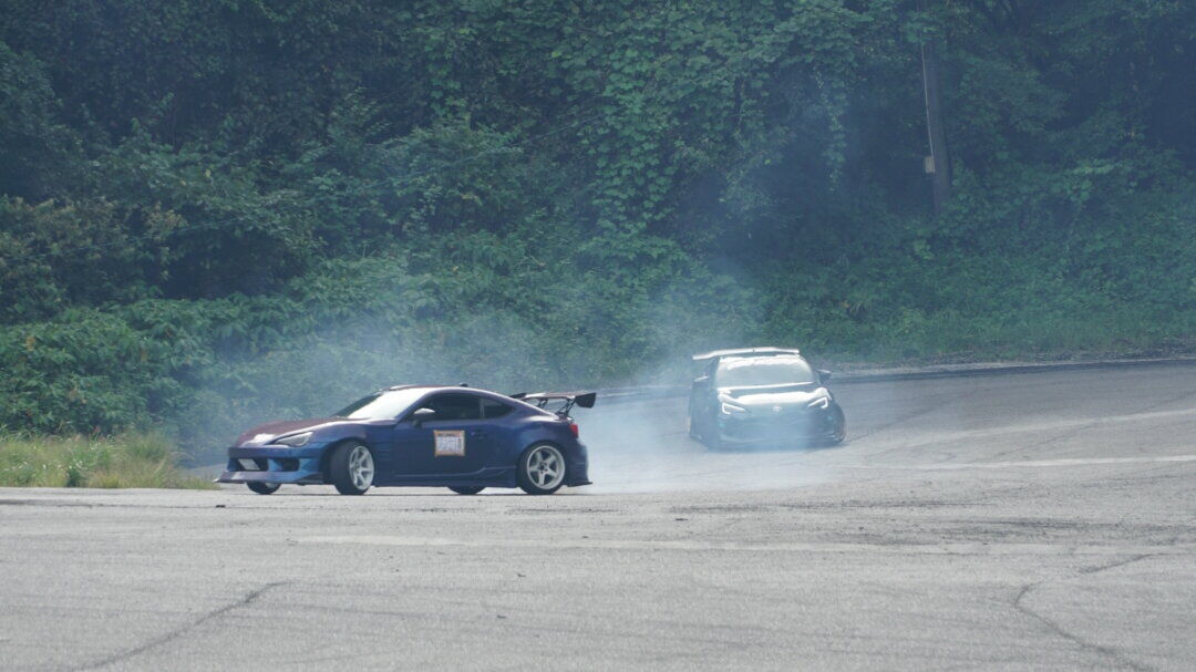 Two drift cars sliding sideways with tire smoke at Ebisu Circuit in Fukushima
