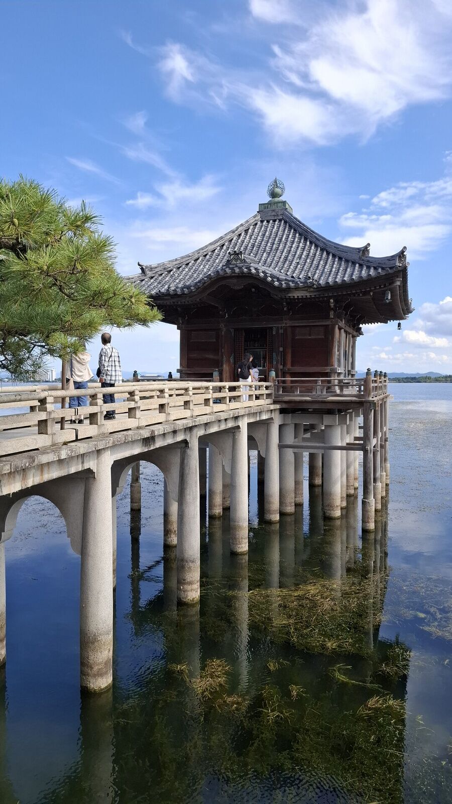The Ukimido seen from the side, stone pillars reflected in the water, a visitor crossing the bridge
