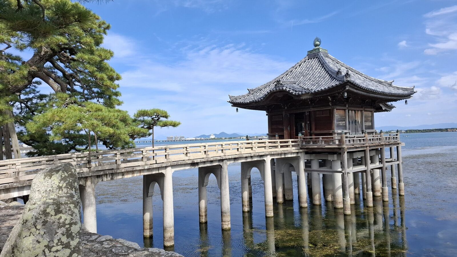 The complete Ukimido composition from shore: pine tree, stone bridge with pillars, floating pavilion, and Lake Biwa beyond