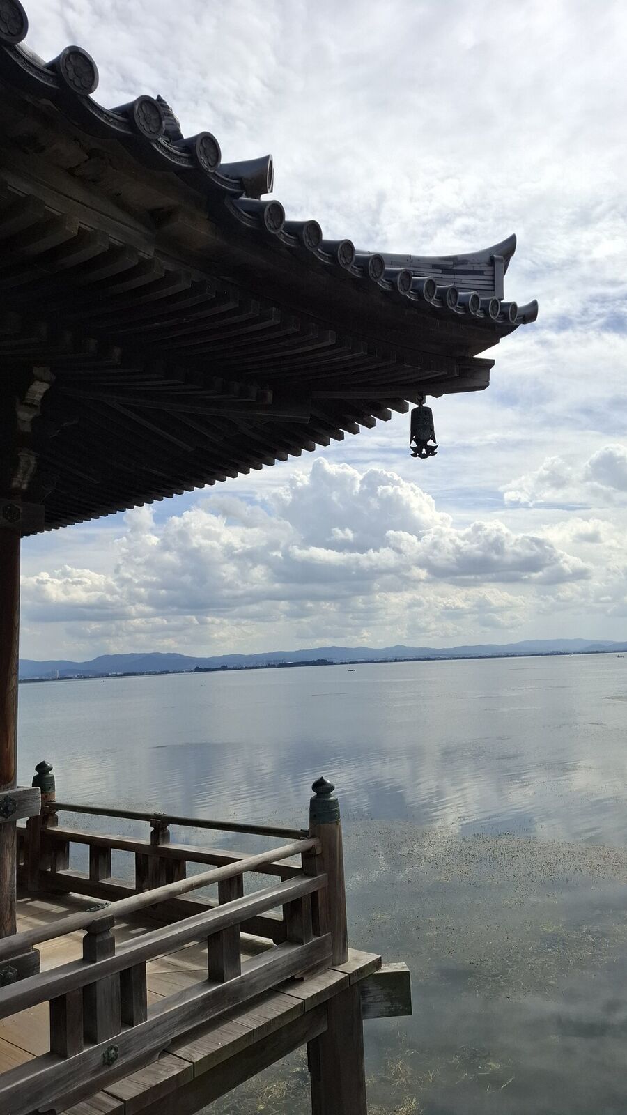 The Ukimido roof ridge and ornamental finial against Lake Biwa and distant mountains, clouds building over the far shore