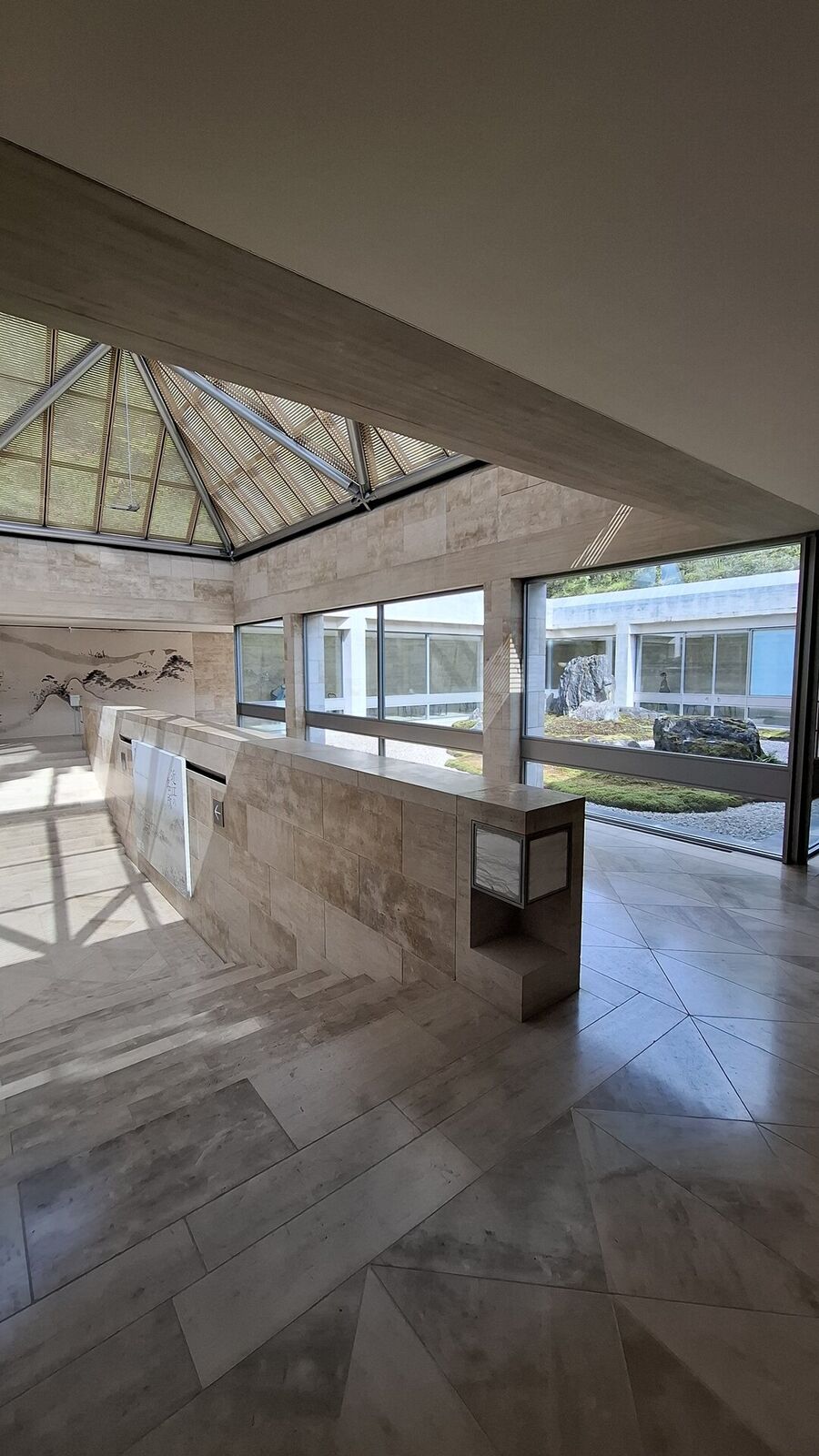 The limestone corridor leading past ink paintings on the walls, glass ceiling above, zen garden visible through the windows at the end