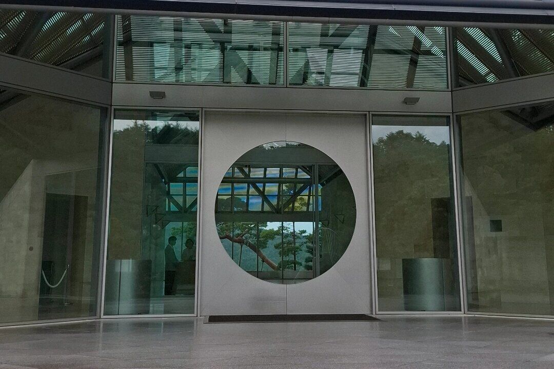 The museum entrance with its iconic circular window framing a Japanese pine branch, set in a limestone and glass facade