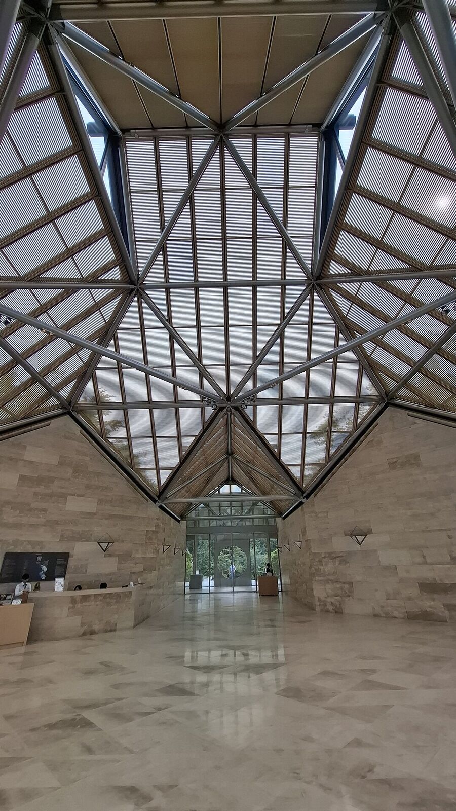 Looking up into the geometric star pattern of the museum's glass and steel roof, limestone walls glowing with natural light, the corridor stretching into the building