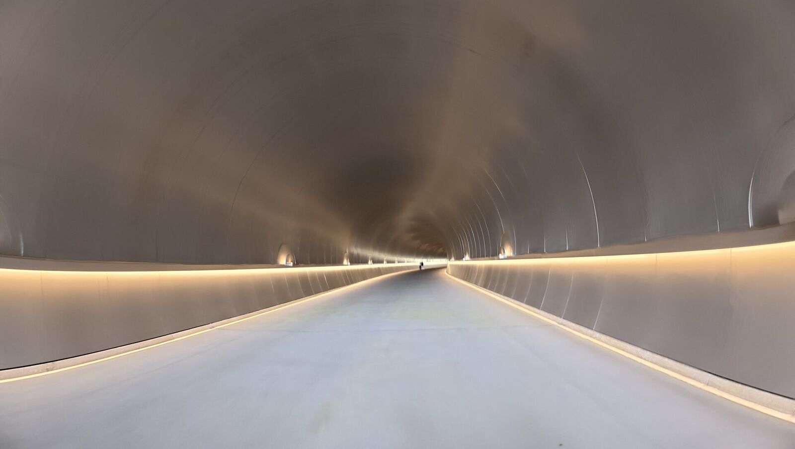 Inside the Miho Museum approach tunnel, copper-clad walls curving into the distance with warm light strips along the floor
