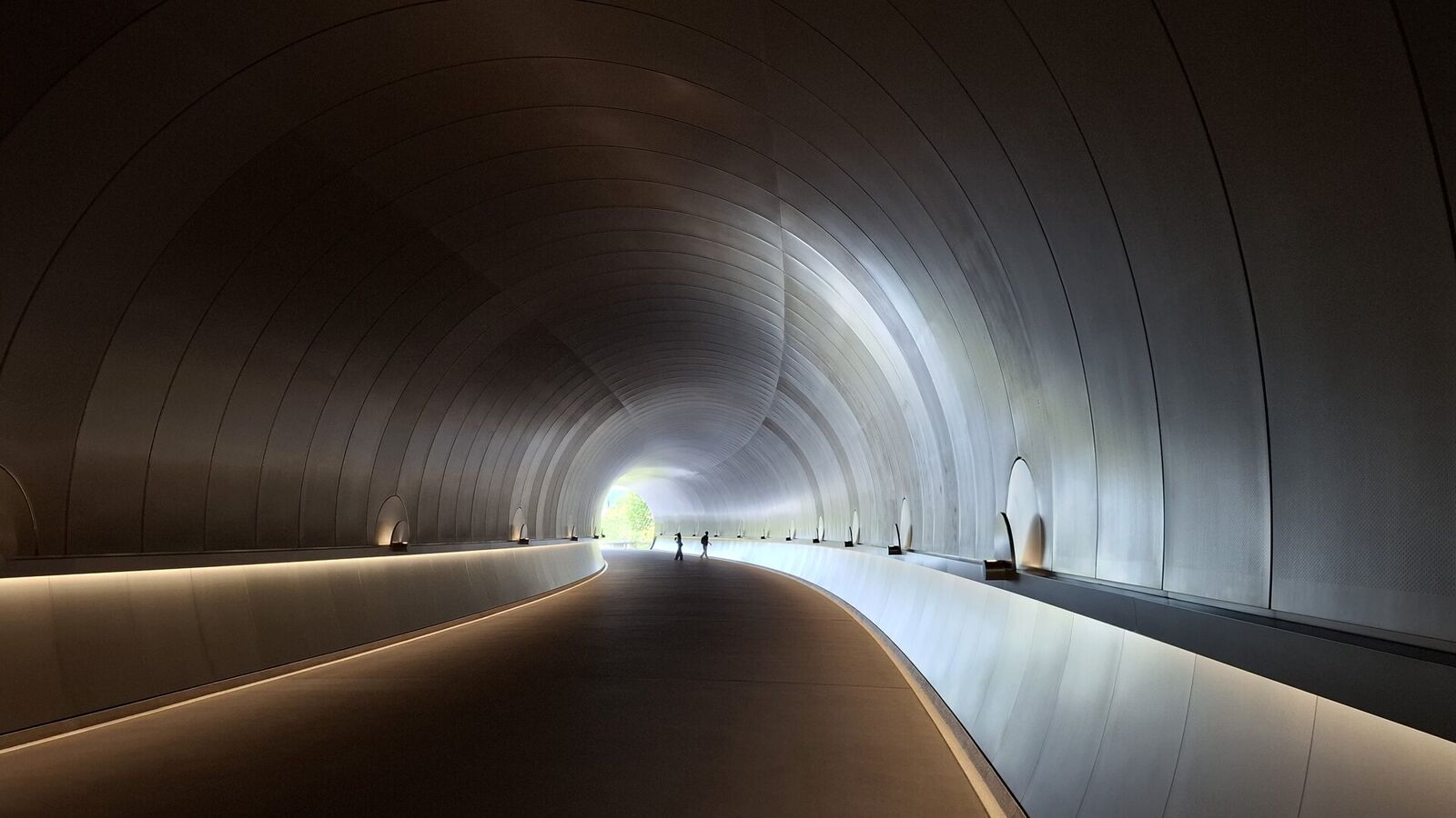 Looking back through the tunnel on the return walk, the copper walls glowing with reflected light, figures silhouetted in the distance