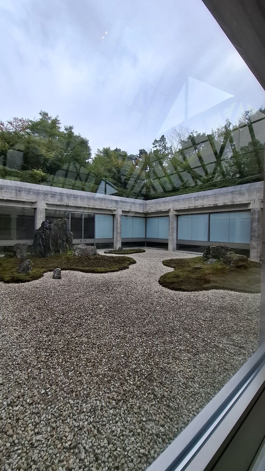The zen garden seen through the glass roof structure, gravel and sculptural moss islands framed by the museum architecture