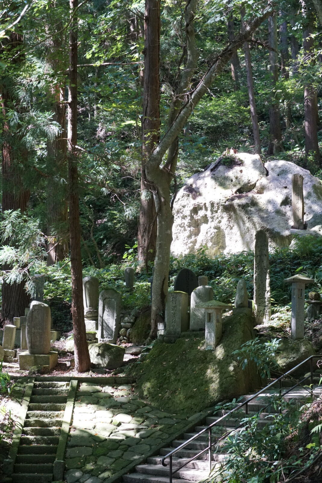 Stone monuments and memorial markers among massive boulders in the cedar forest, showing the depth of history along the path