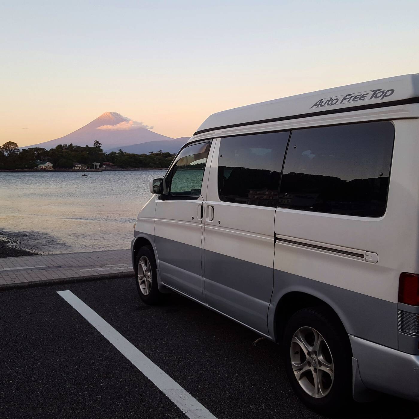 Campervan parked at the coast with Mount Fuji across the bay at sunset
