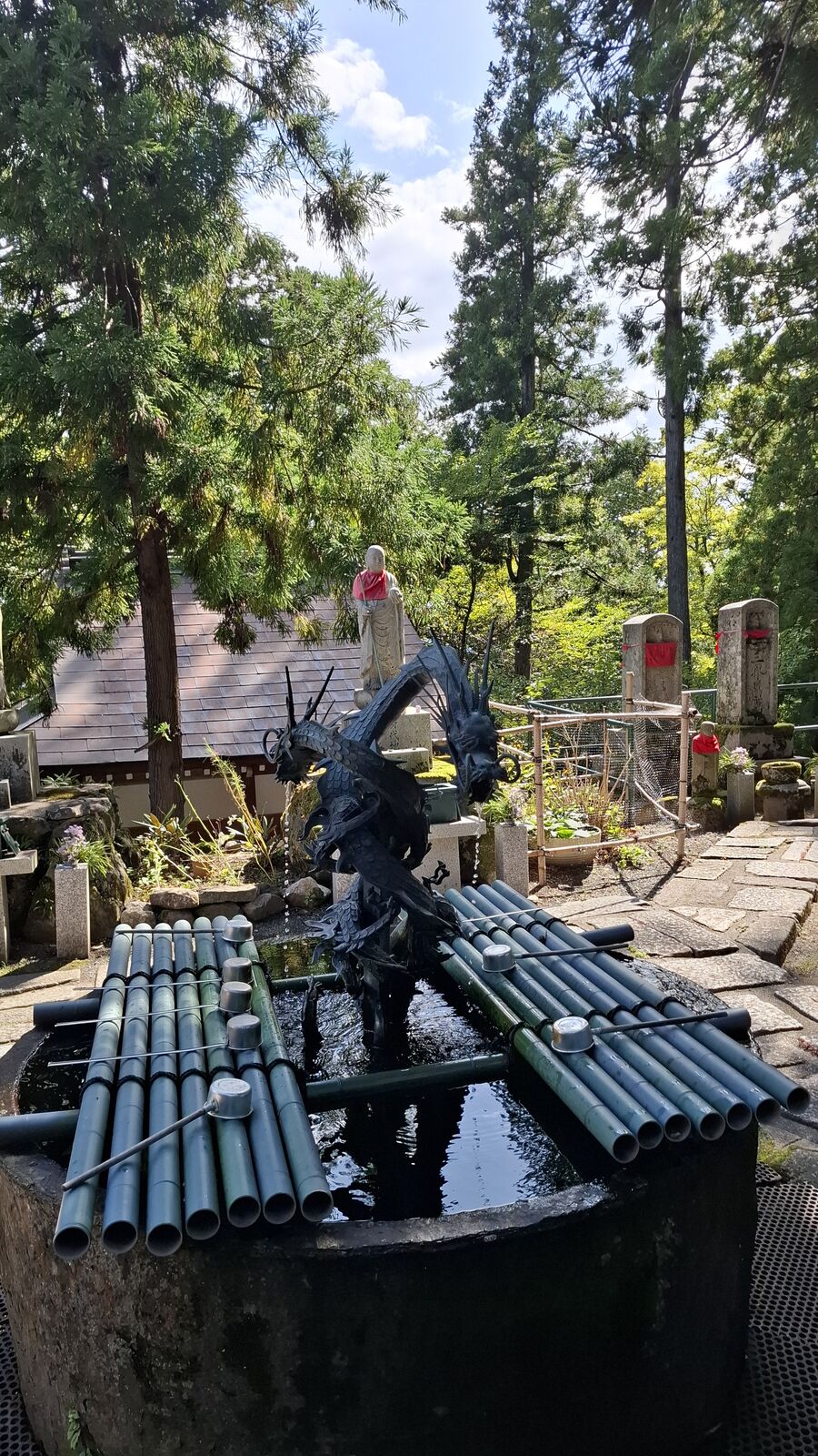 A dragon statue guarding the entrance of Nariaiji temple, surrounded by bamboo ladles and offerings, with the temple roof visible above
