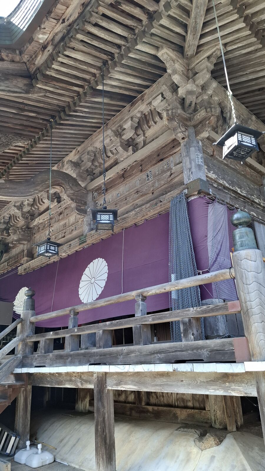 Looking up at the ornate wooden ceiling and bracket structure of Nariaiji's main hall, massive beams and traditional joinery under purple ceremonial curtains