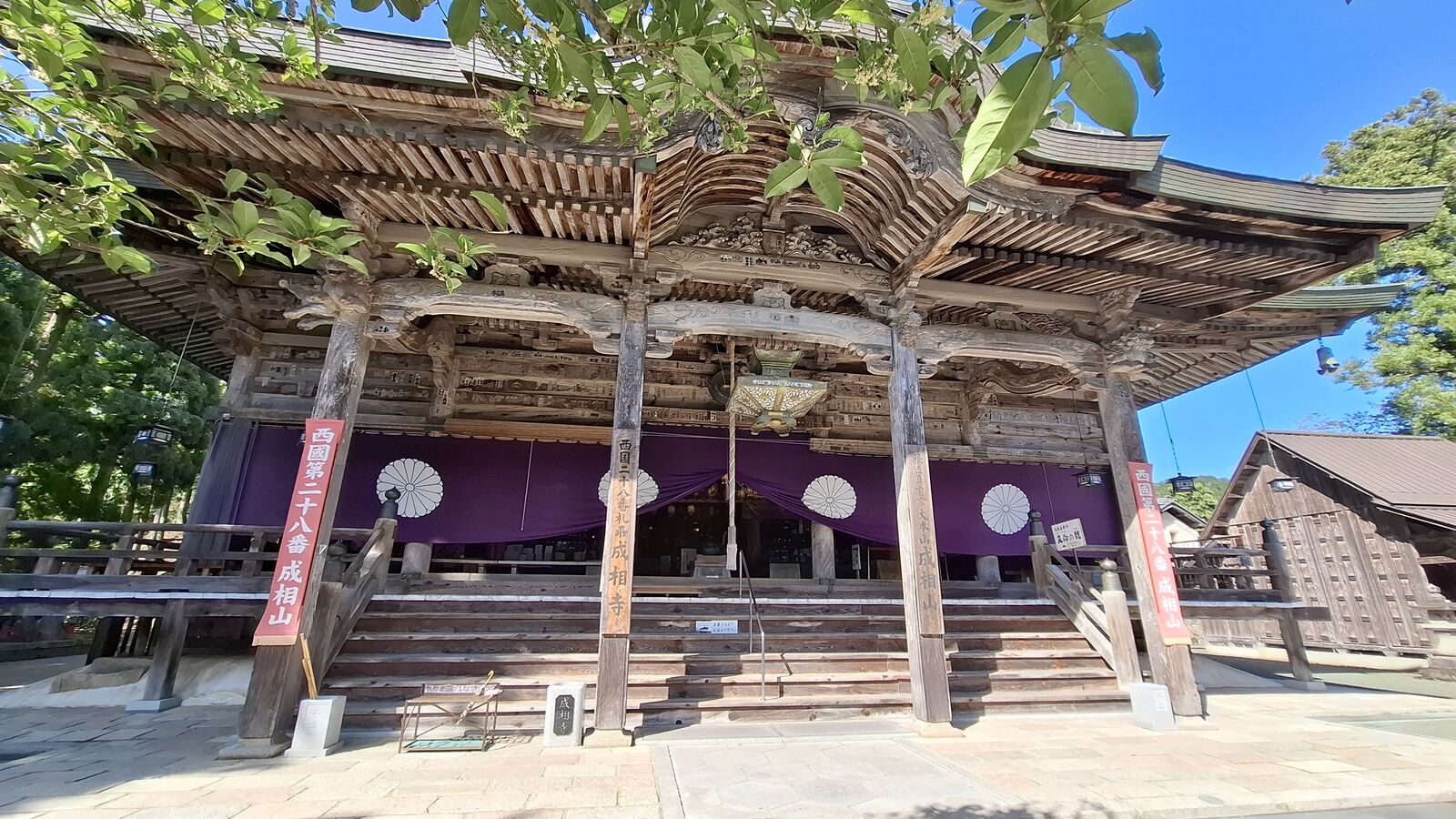 The main hall of Nariaiji temple, massive wooden columns and exposed joinery, purple curtains with white chrysanthemum crests hanging across the facade