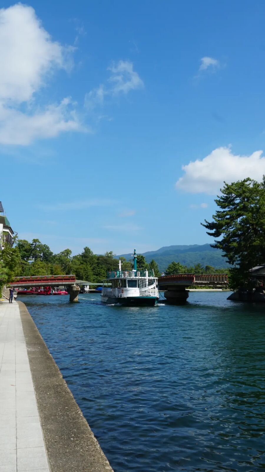 View from the rotating bridge toward Amanohashidate, a tour boat passing under the bridge with mountains in the background