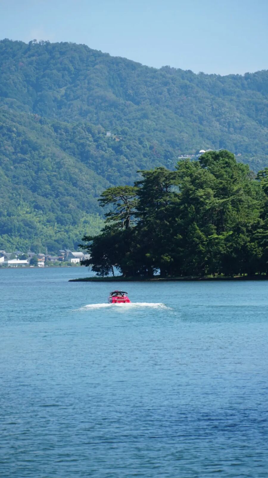 A red speedboat crossing the bay near Amanohashidate with forested mountains rising behind
