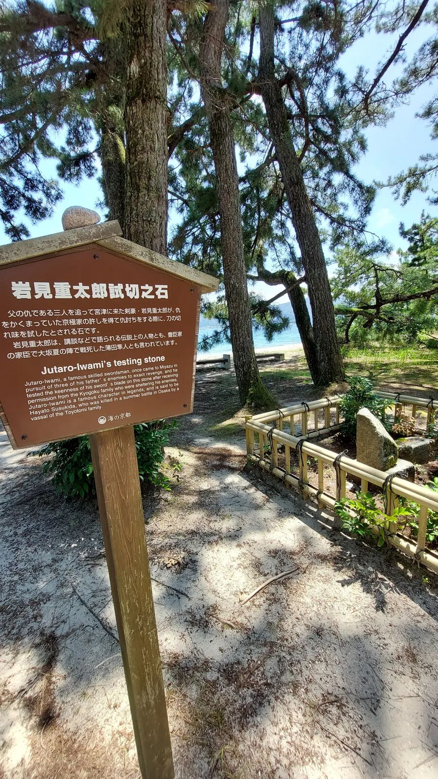 Iwami Jutaro's sword-testing stone on Amanohashidate, a wooden information sign in Japanese and English beside the split boulder behind a wooden fence