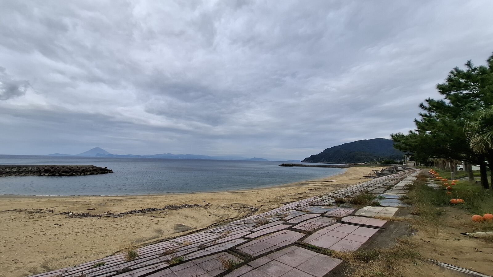 Sandy beach on the southern Kyushu coast with mountains fading into clouds in the distance, a stone boardwalk leading along the shore