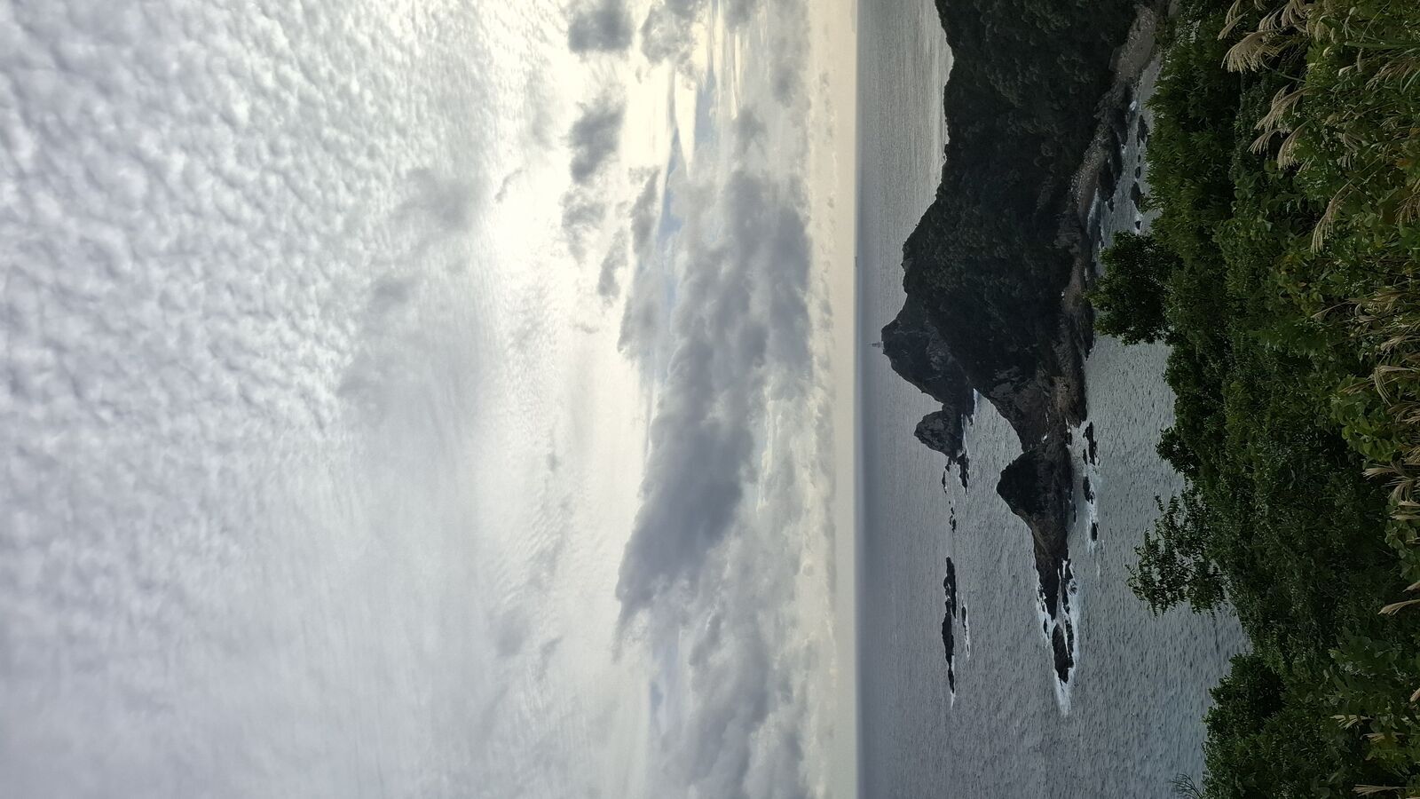 Steep cliffs dropping into the ocean, waves breaking against rocks below, seen from the approach path to the cape