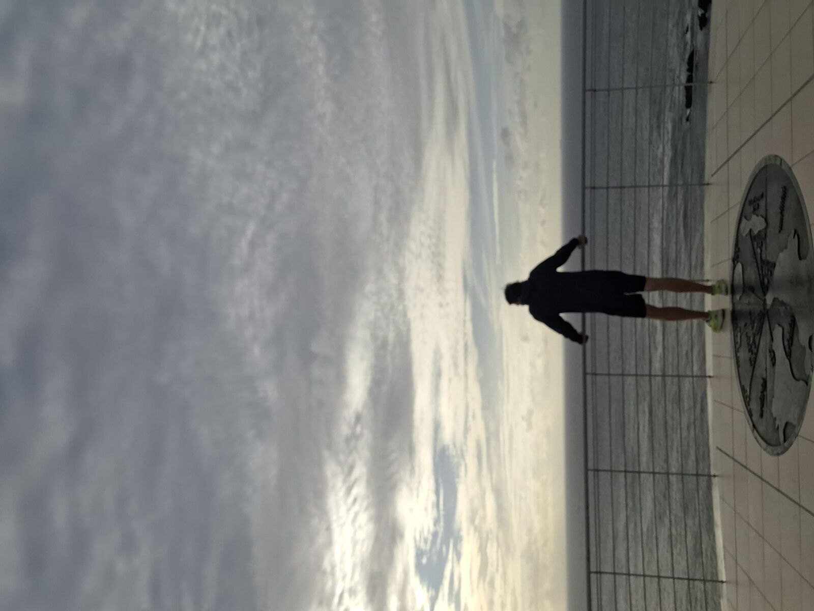 Kevin's silhouette on the observation platform, standing at the compass marker, ocean and sky stretching to the horizon