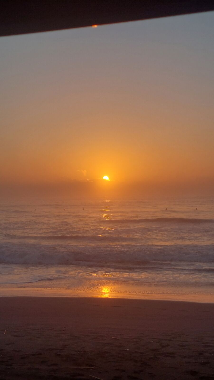 Pure golden sunrise over the Pacific Ocean seen from behind the van's windshield frame, warm light flooding the beach