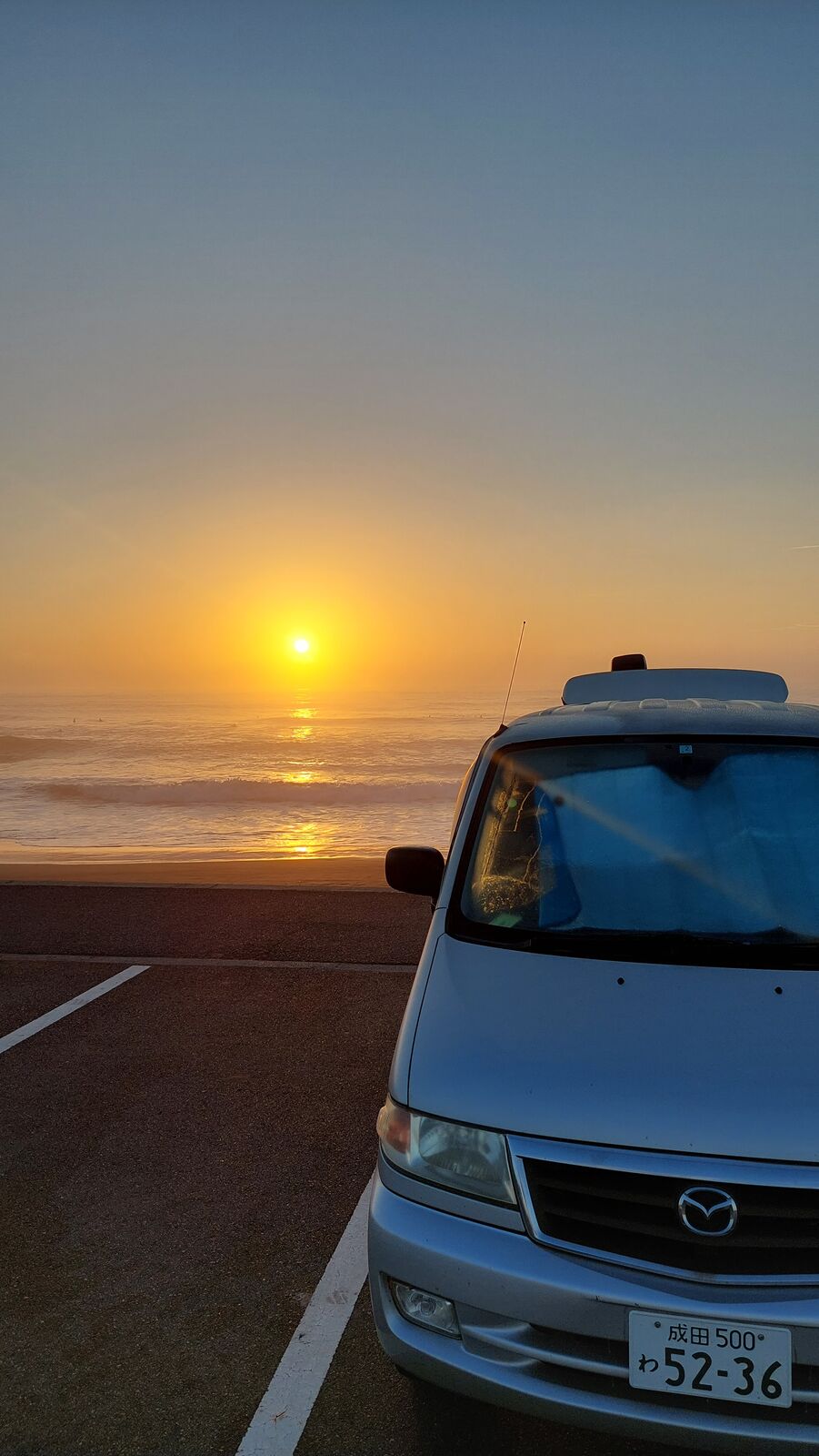 Mazda Bongo campervan front with Narita rental plates, sunrise over the Pacific behind, parked at the seawall