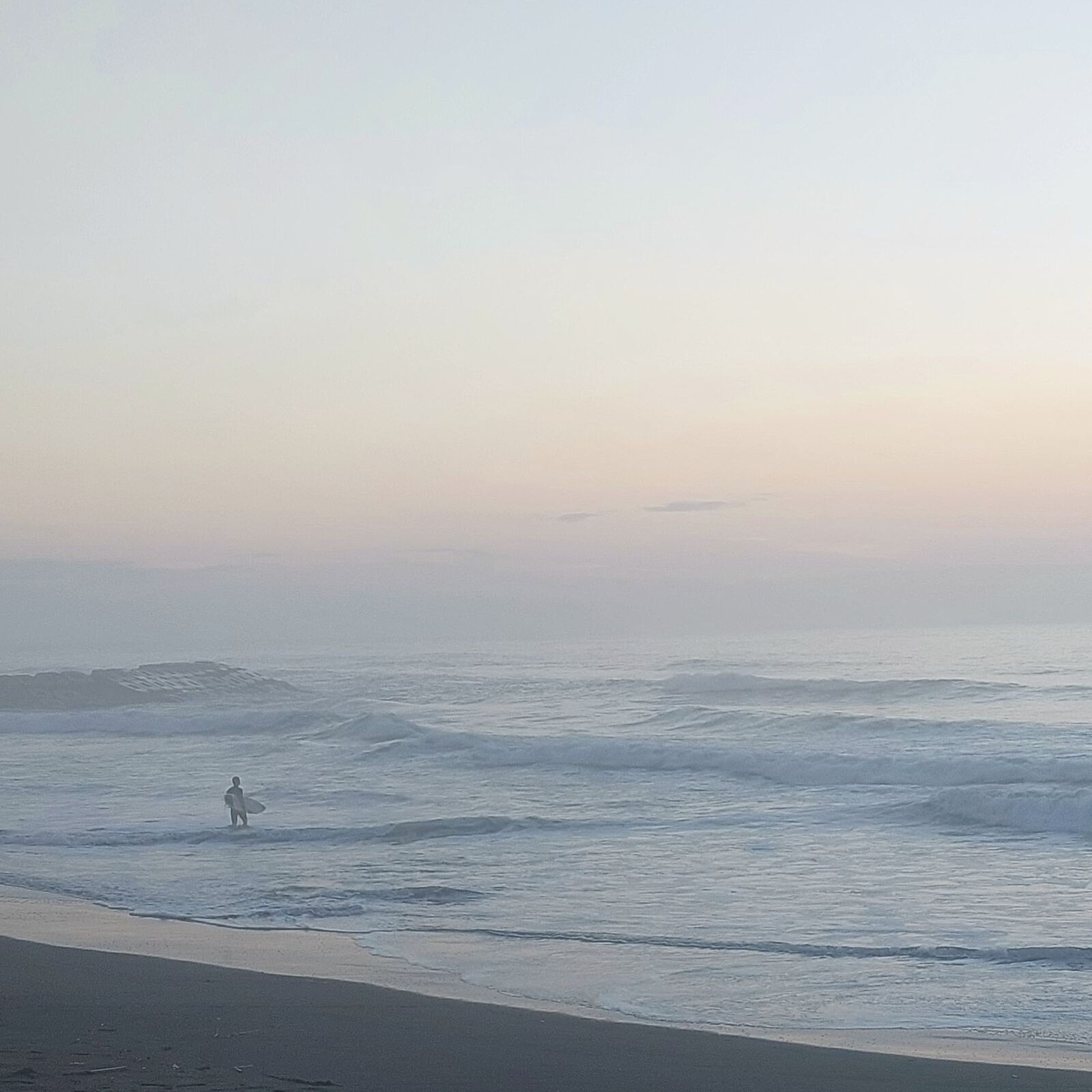 Distant surfer walking on the beach in soft pastel dawn light, minimalist composition with ocean and sky