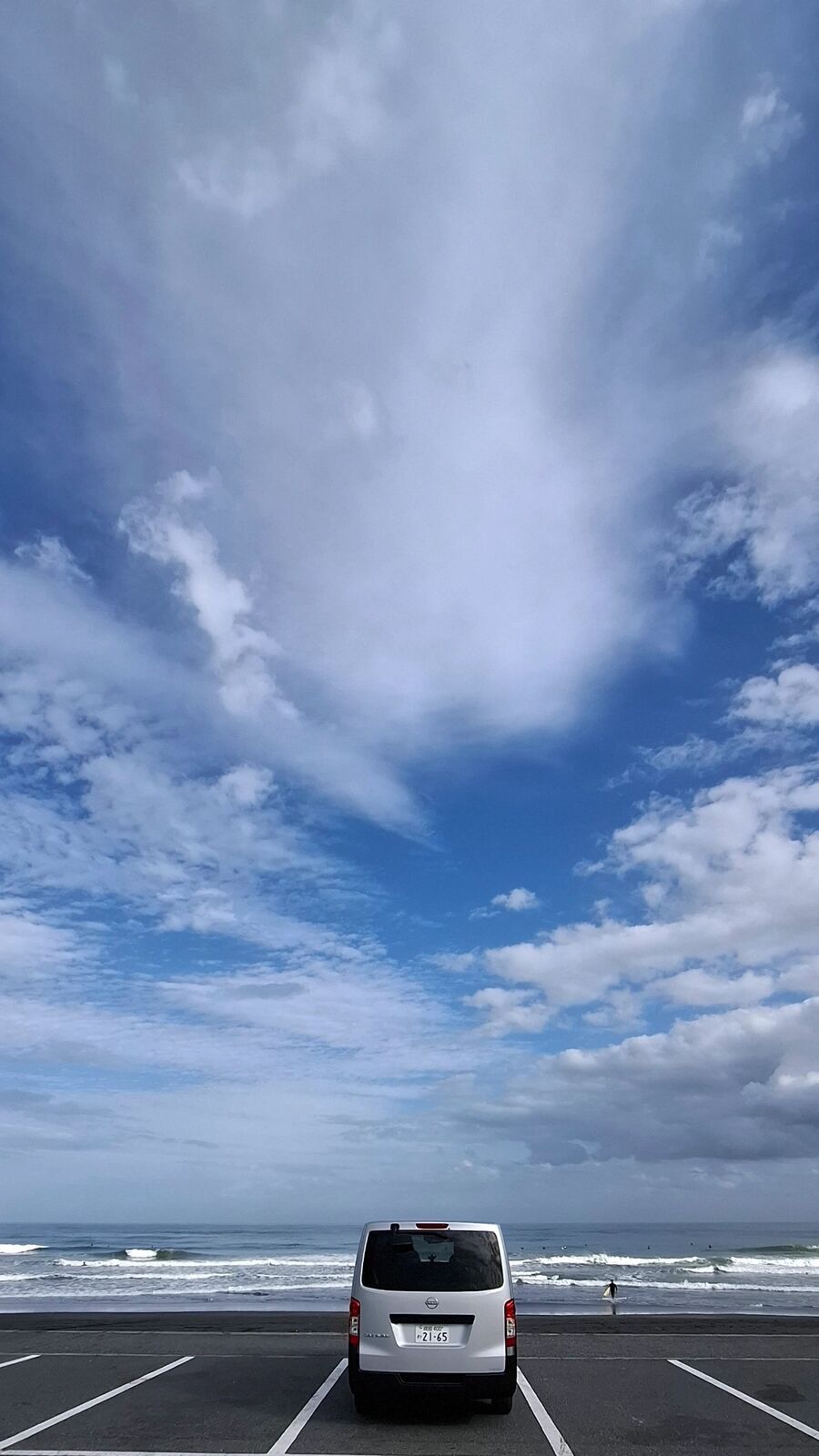 Campervan alone in the parking lot facing the Pacific, dramatic autumn clouds towering above, a solitary figure walking on the beach