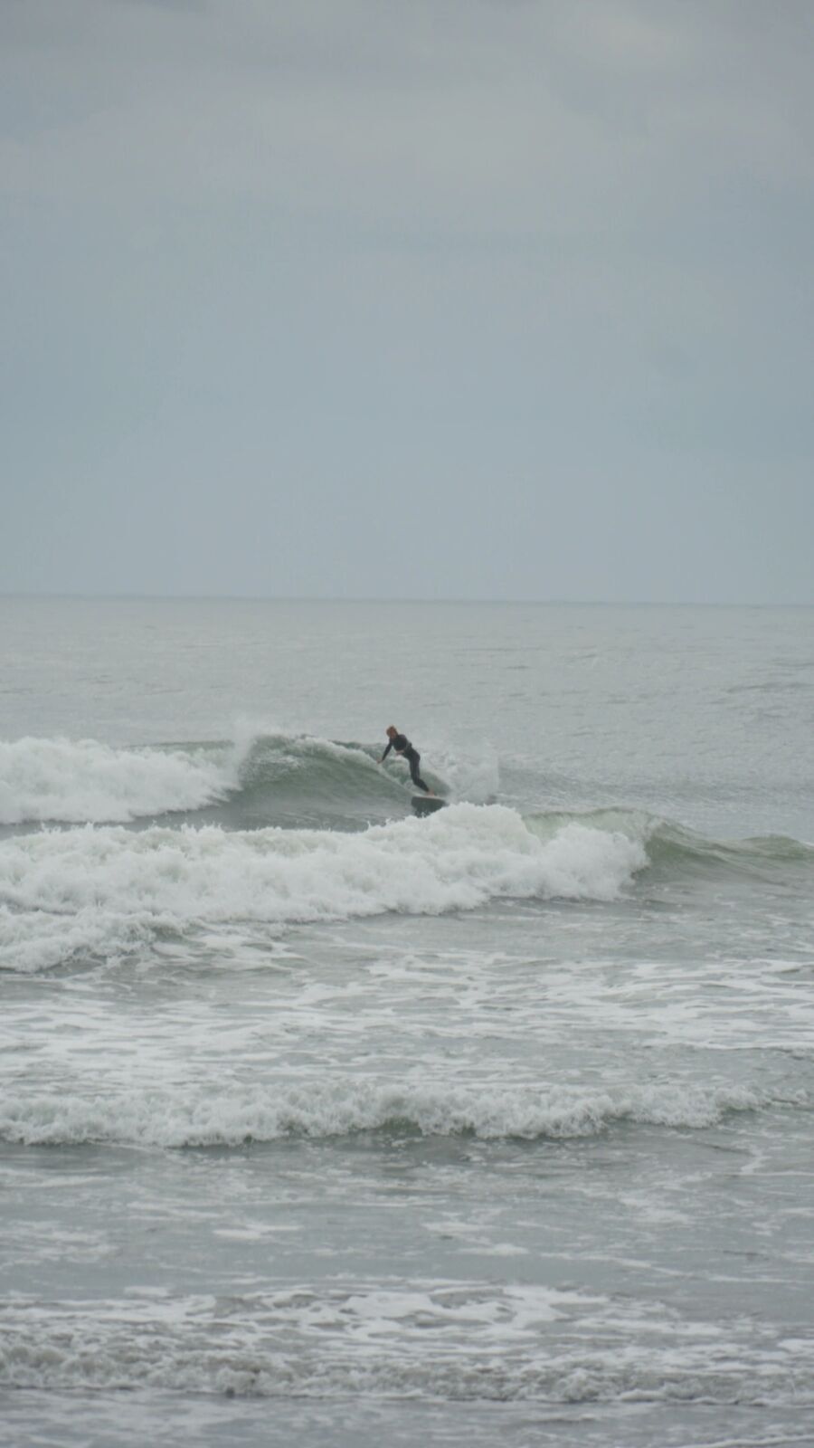 Surfer riding a wave at Kujukuri, overcast autumn sky, white spray and grey-green water