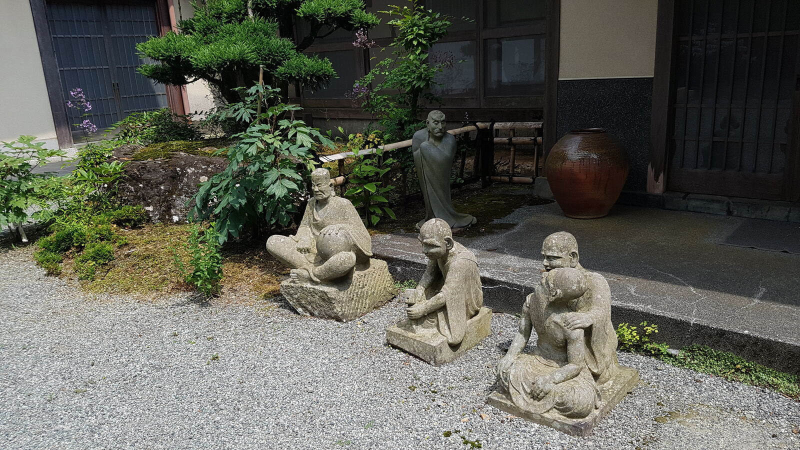 Group of rakan figures in everyday poses at the temple entrance courtyard, a standing figure watching from behind a large pot