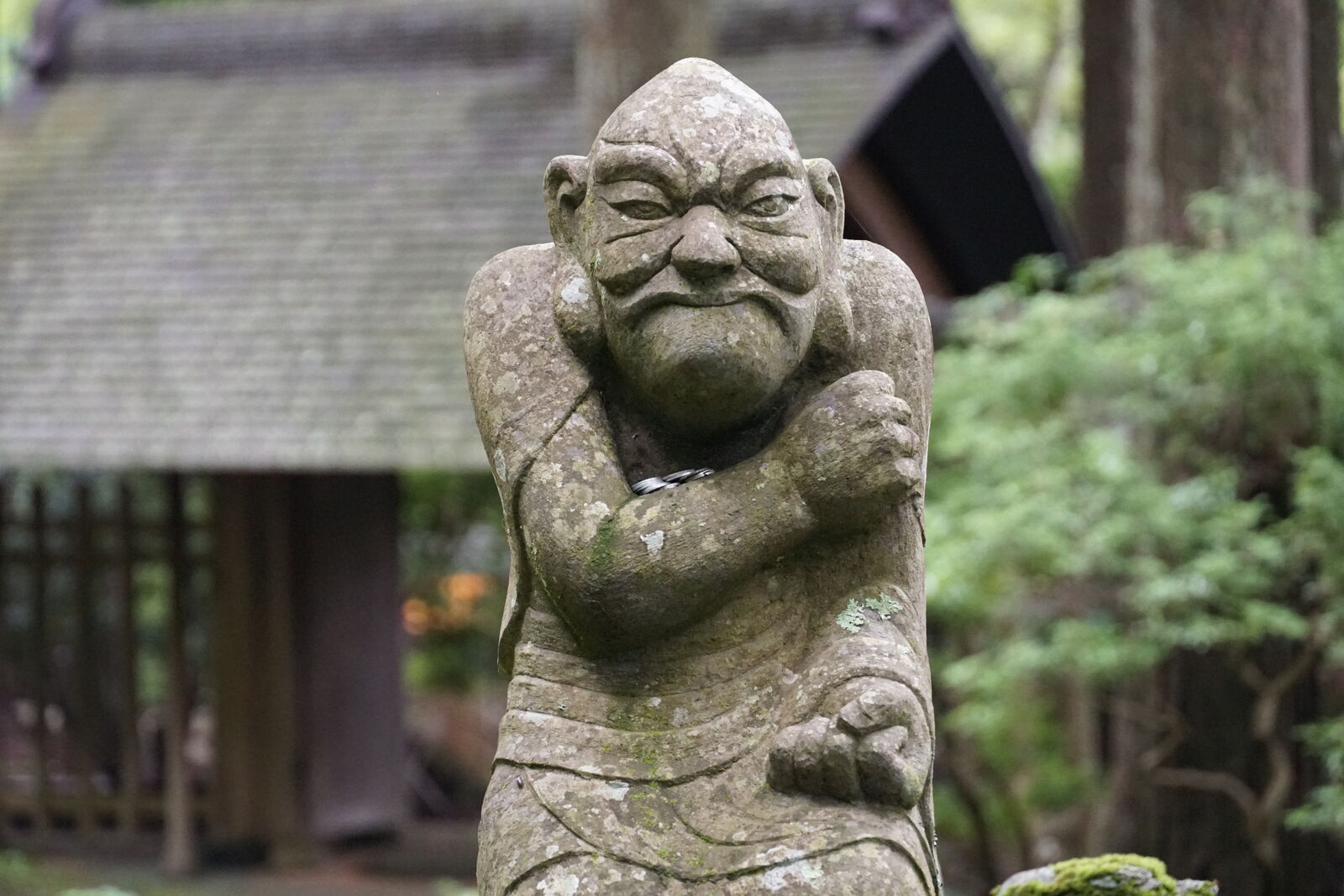 Muscular rakan figure with crossed arms and fierce expression, temple building visible behind
