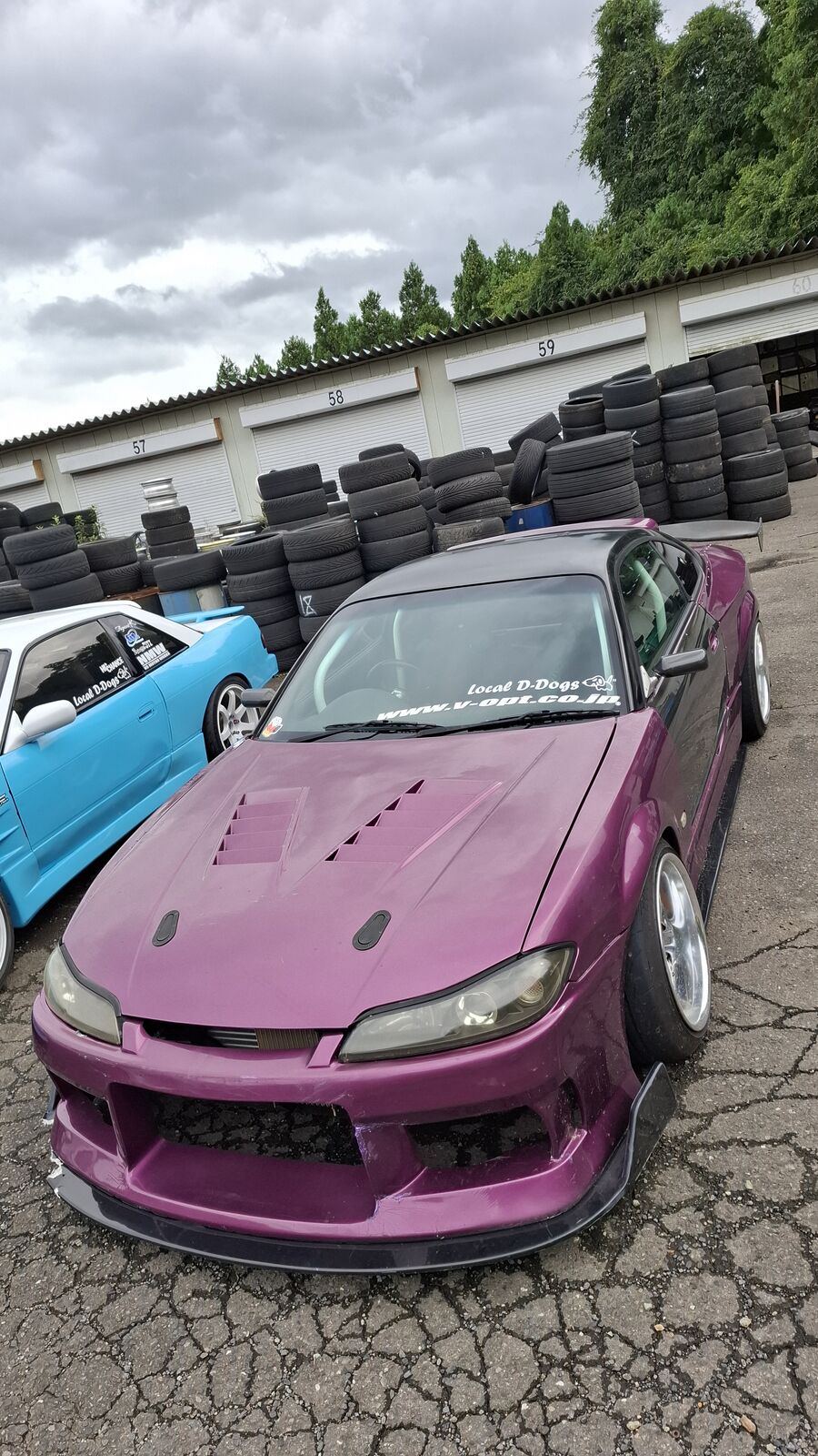 Pink-purple Nissan 350Z next to stacked tires in the parking area
