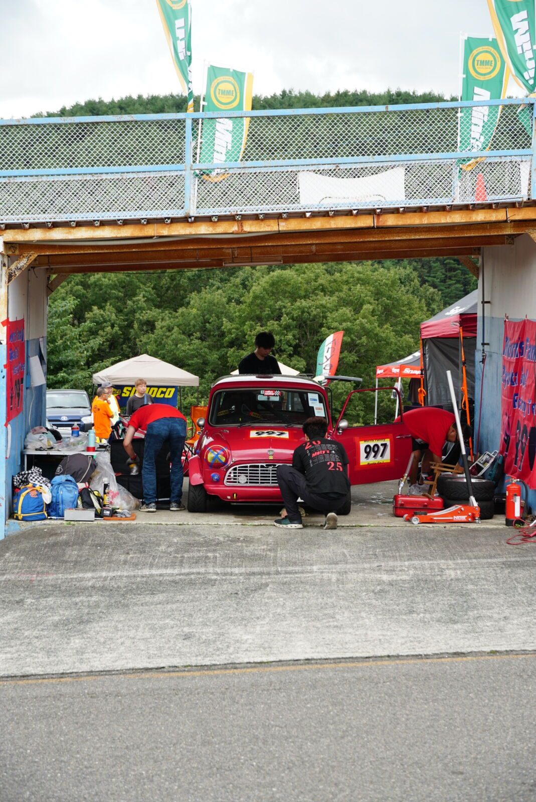 Red classic Mini number 66 in the paddock with Italian flags and racing equipment