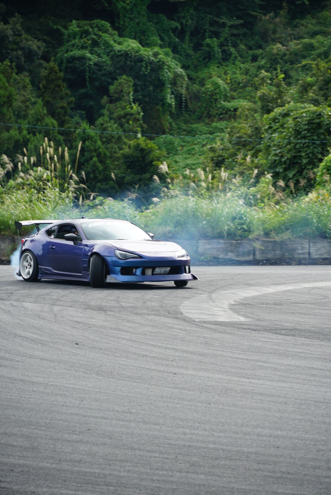 Blue car drifting on the pad with smoke trails on the marked-up surface