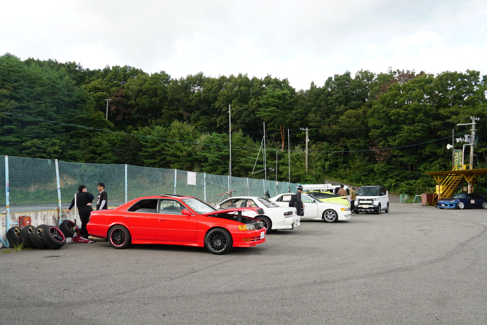 Red Toyota Mark II JZX100 among a mix of drift cars in the paddock with people working on their vehicles