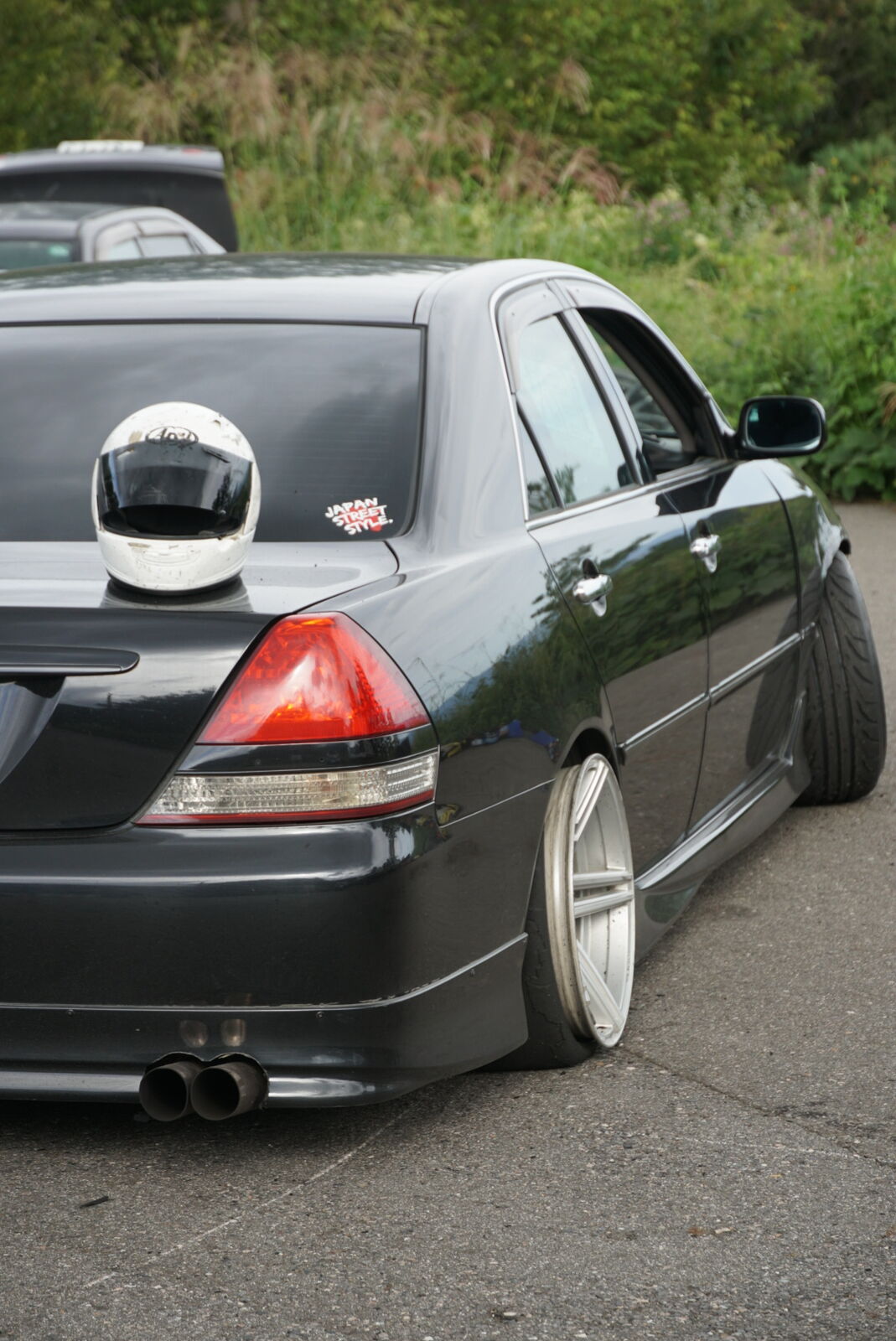 Dark slammed sedan with helmet on the trunk, deep dish wheels, and quad exhaust