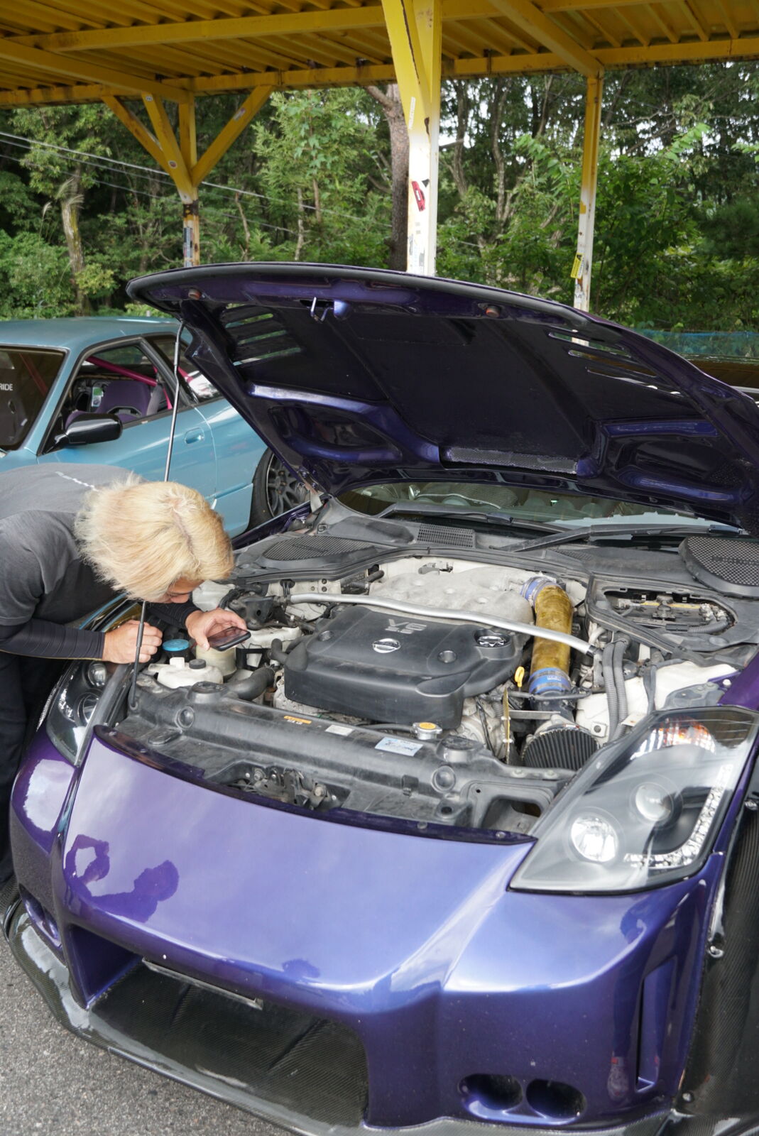 Person working on a purple Nissan Silvia S15 engine bay next to the viewing tower
