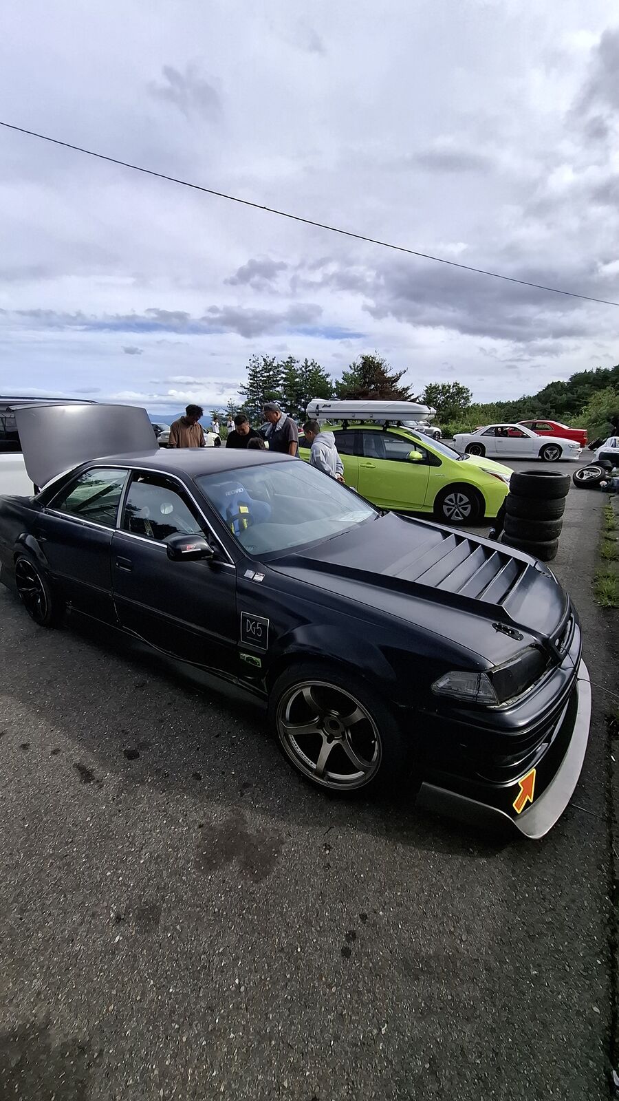 Black modified car with lime green vehicle visible behind it