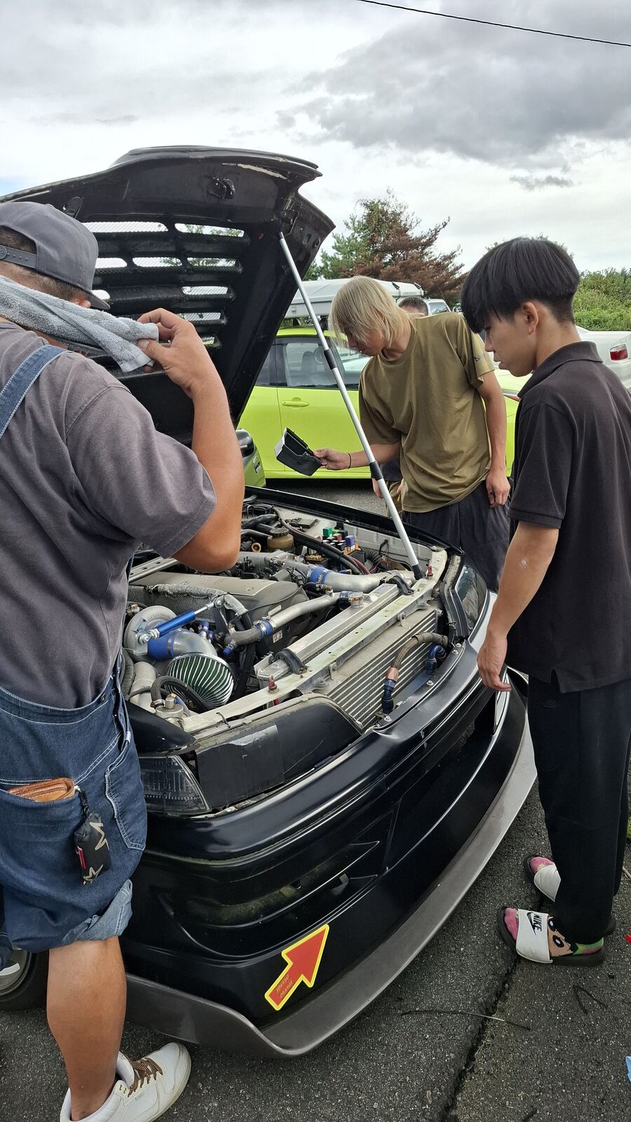 Group of people gathered around an open engine bay, inspecting and discussing the build