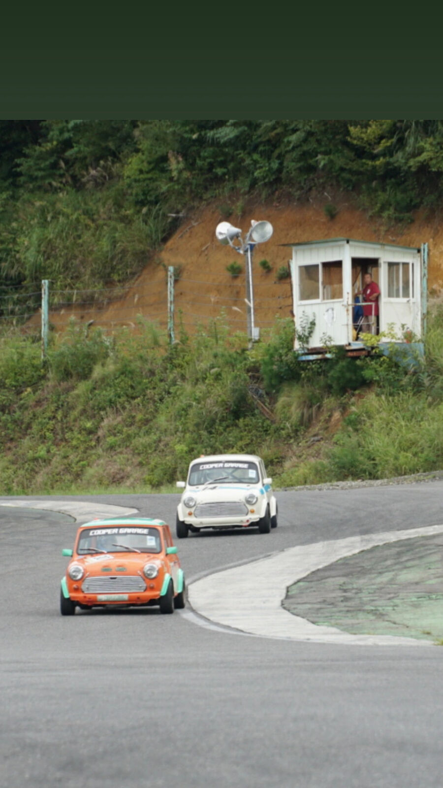 Orange and white classic Minis racing past the hillside guard hut