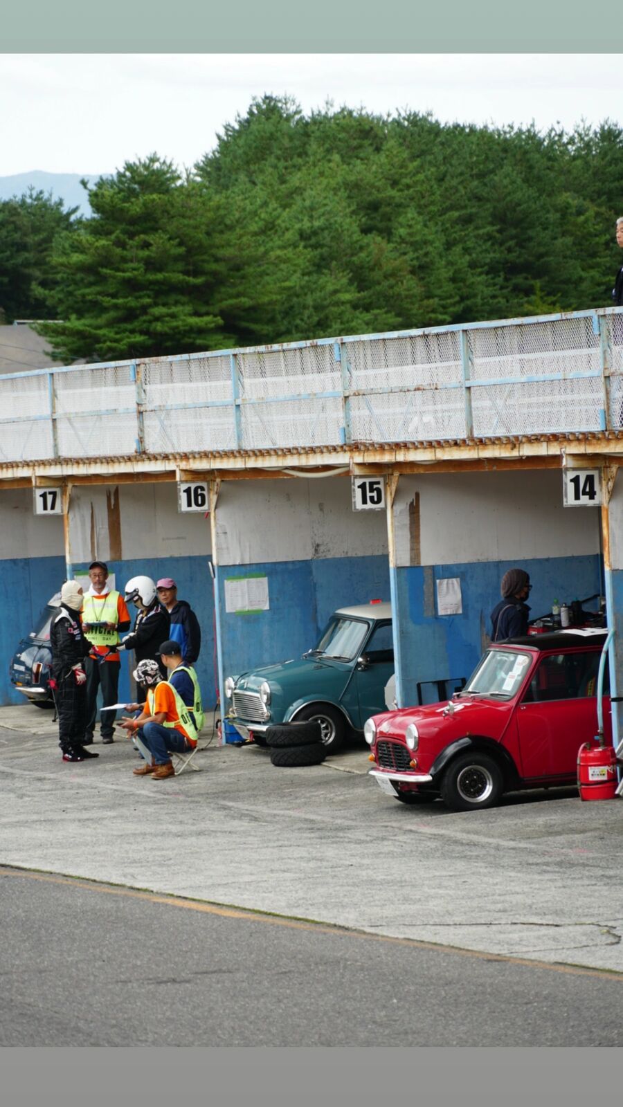 Classic Minis parked in numbered pit bays with people working on their cars