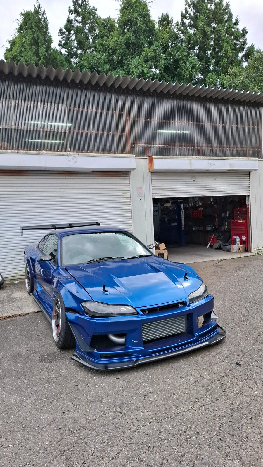 Blue widebody Nissan Silvia S15 parked in front of workshop garages