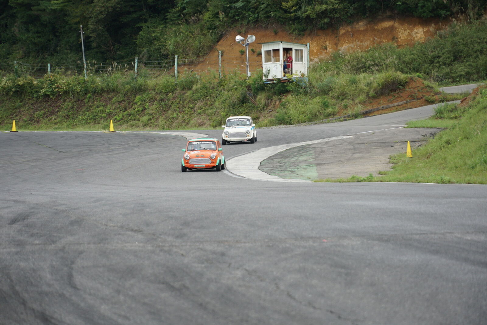 Orange and white Mini side by side on the hillside circuit