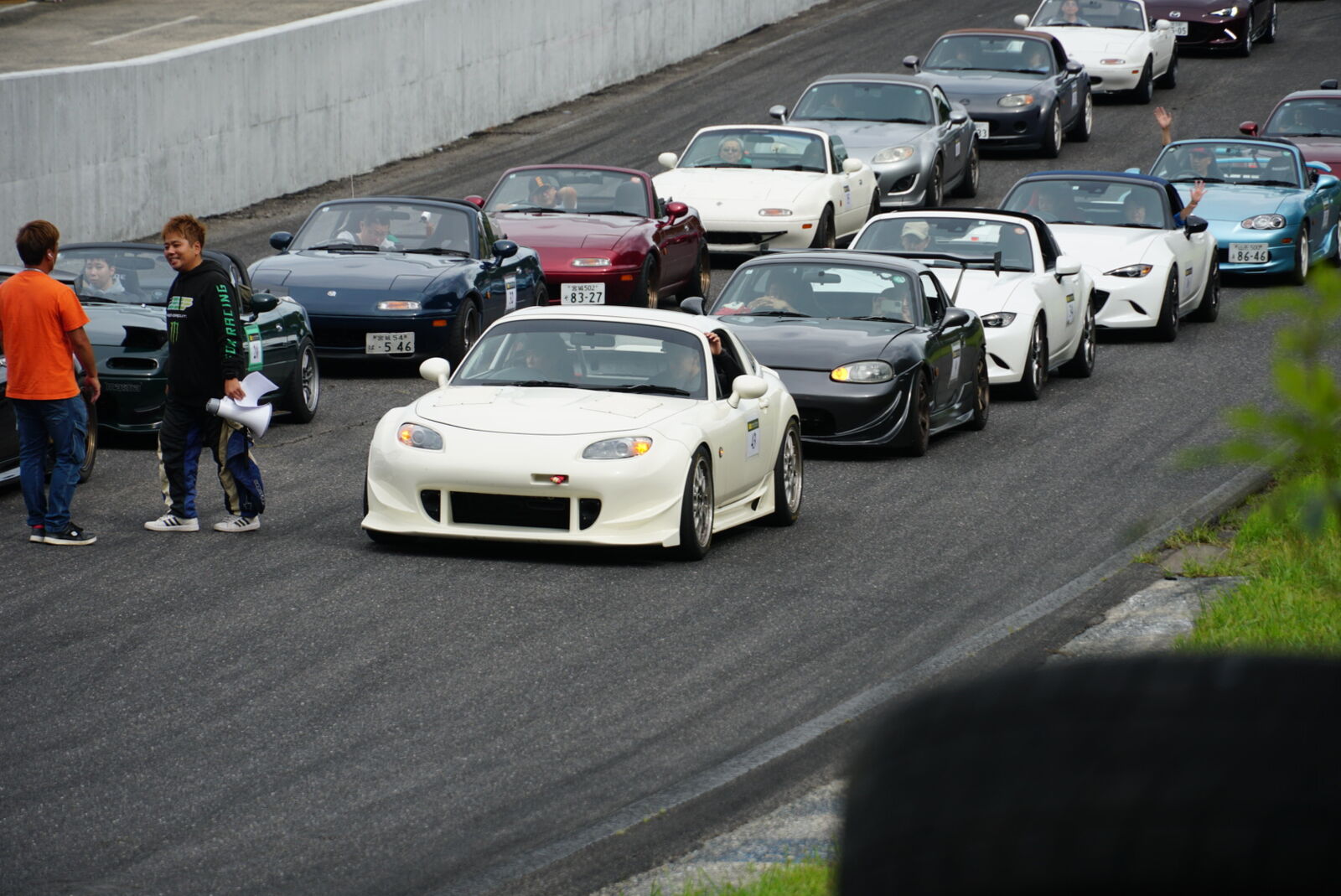 White car parked among the gathering with the circuit in the background