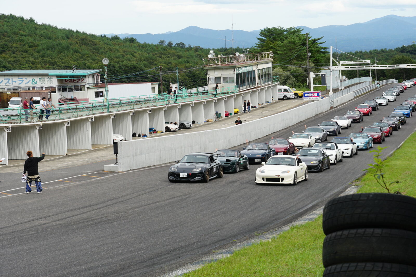 Elevated view across the circuit with mountains in the background and cars on track below