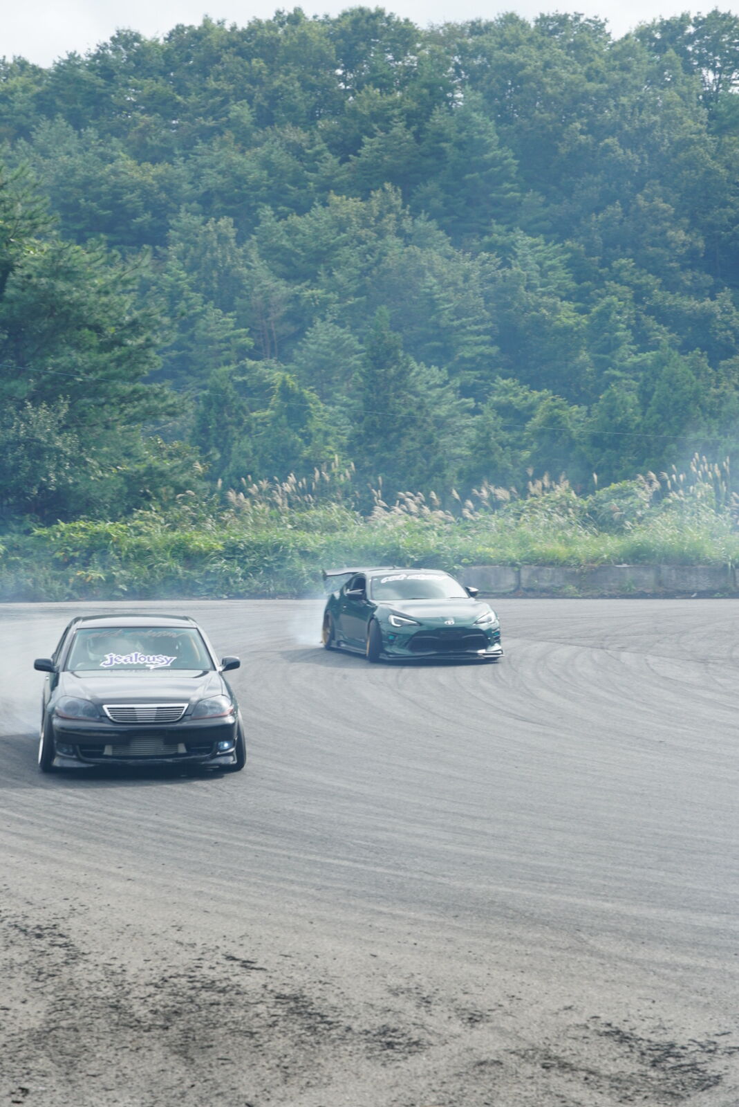 Black car sideways with tire smoke billowing across the drift pad