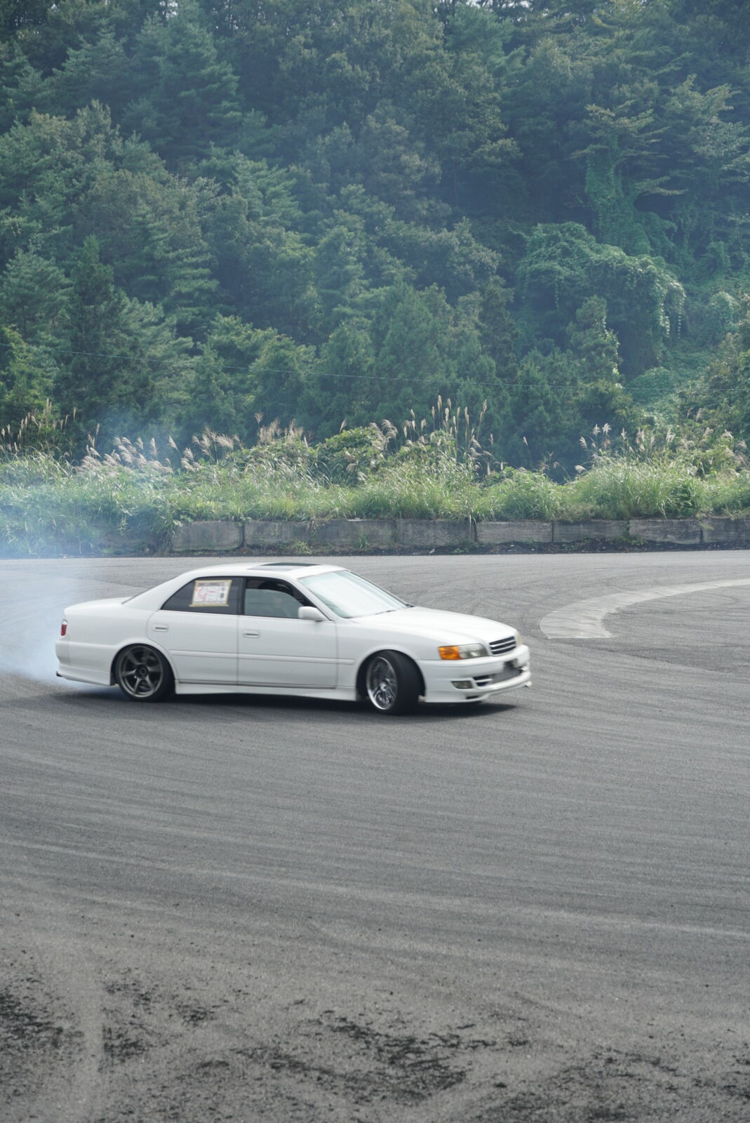 White sedan throwing up a huge cloud of smoke mid-drift