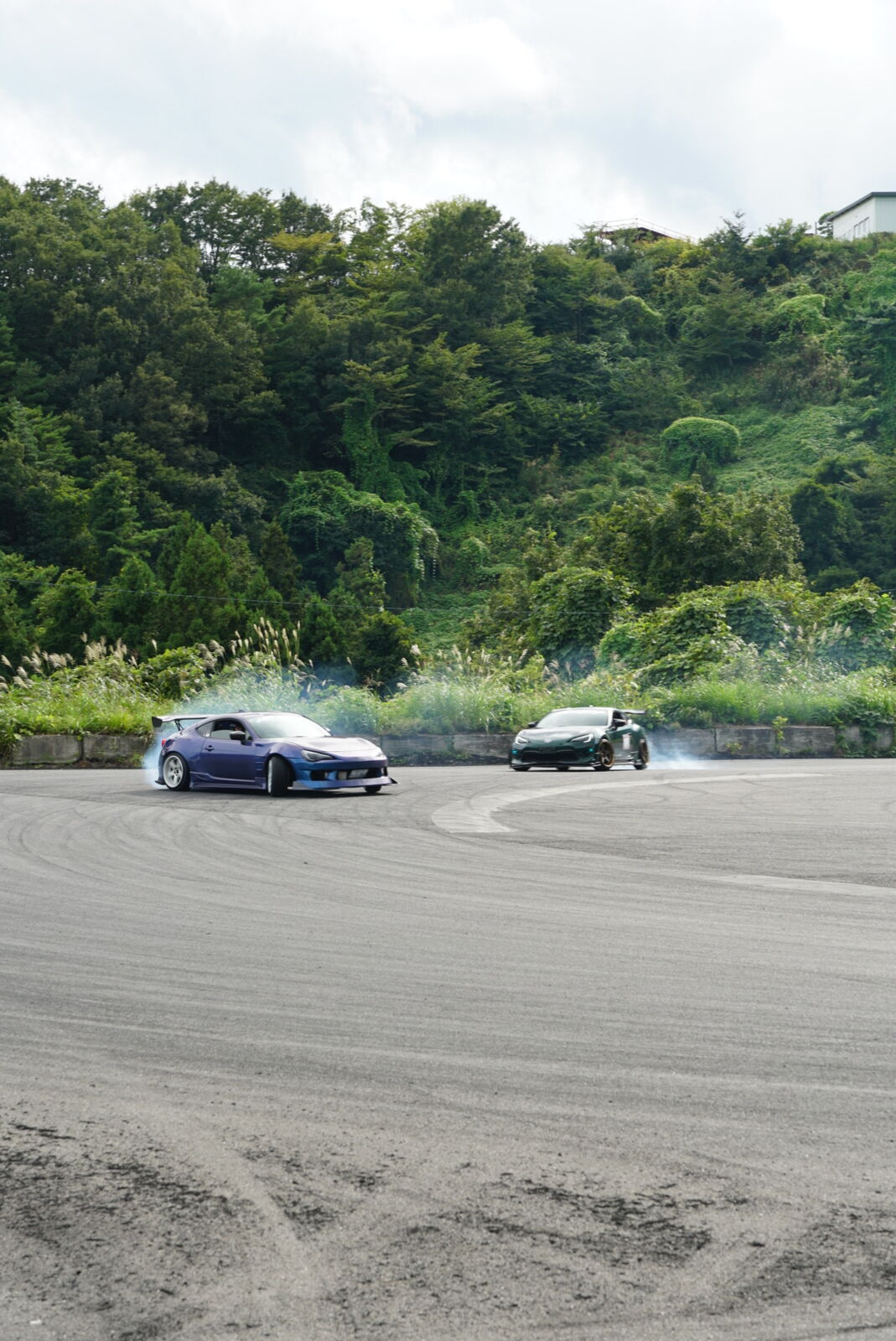 Two cars in close tandem drift formation with overlapping smoke trails
